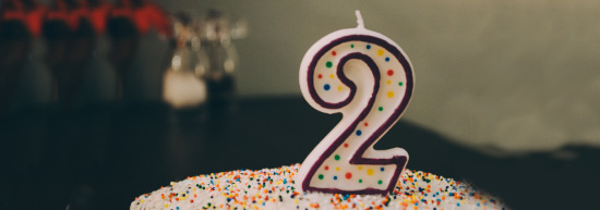Ein Geburtstagskuchen auf dem eine Kerze steht. Die Kerze hat die Form der Zahl "2"